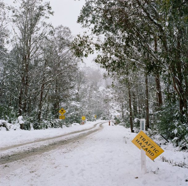 Snowy road into Devils Gullet with caution signs on Kodak Portra 400 by Jade Austen